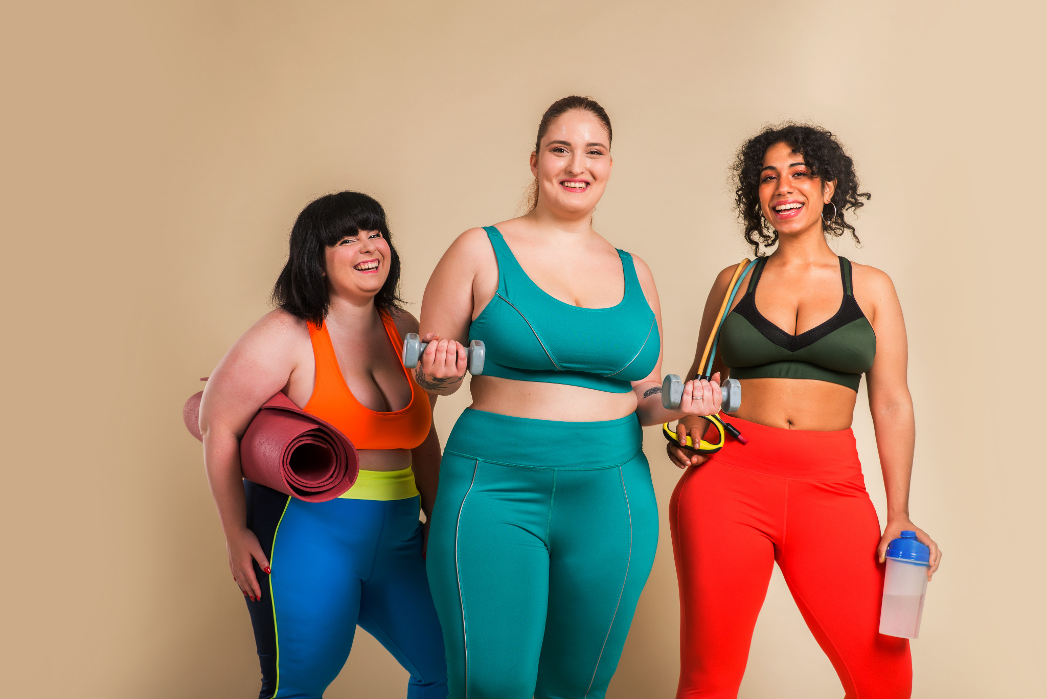 Three women in colorful workout clothes smiling together.