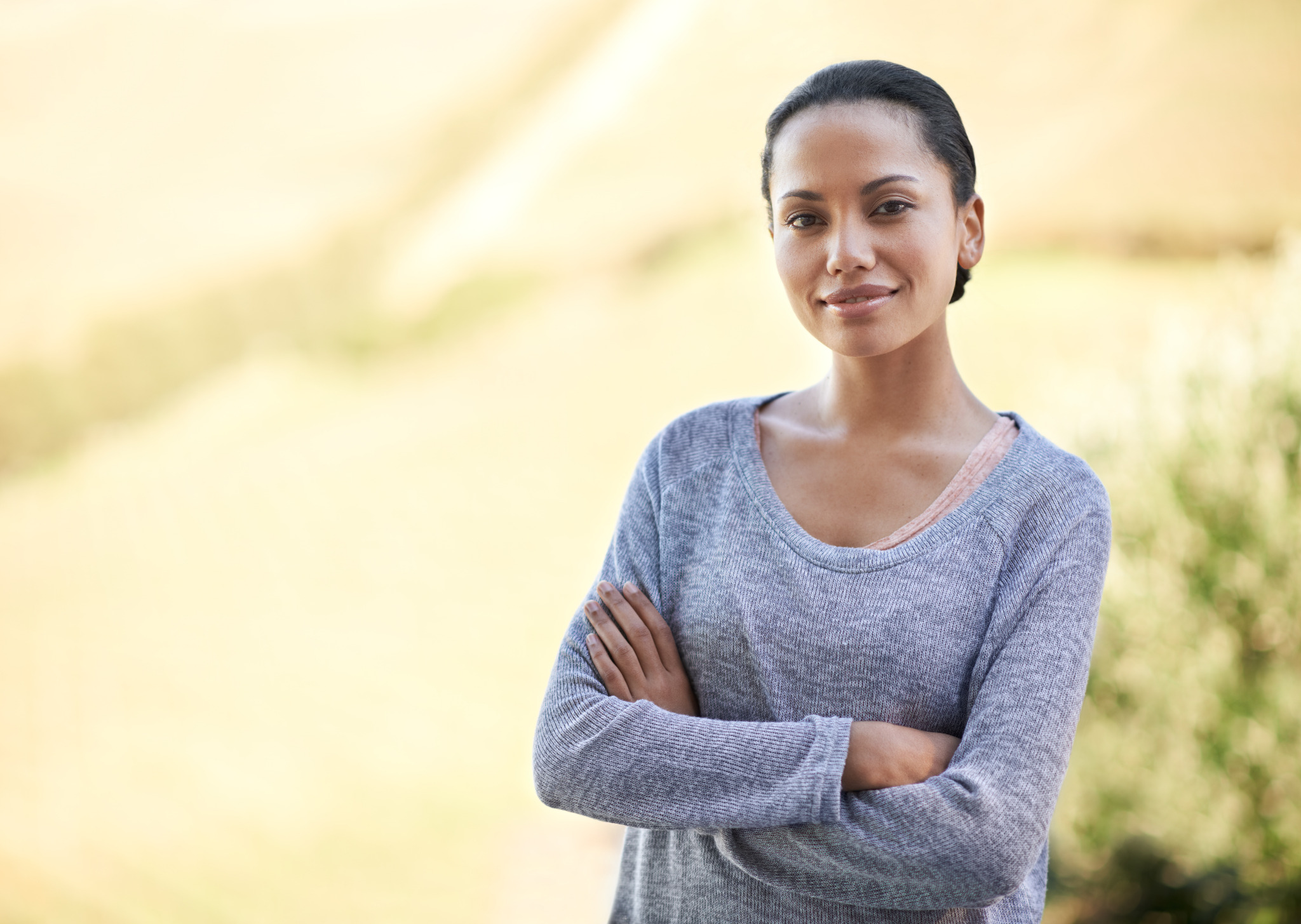 A woman standing outdoors with her arms folded and a calm, confident expression.